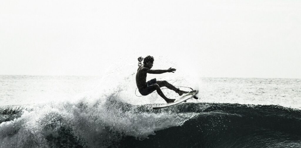 A surfer on a left-hand wave in black and white, performing a turn with fins out and a spray of water