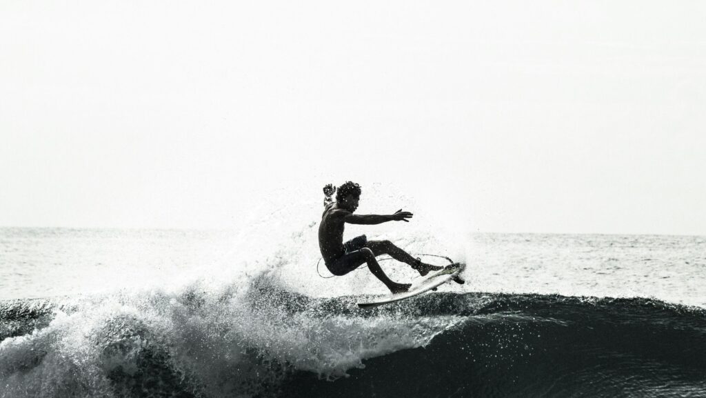 A surfer on a left-hand wave in black and white, performing a turn with fins out and a spray of water
