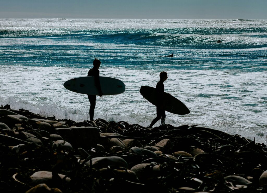 Two surfers holding their boards, standing on rocks, about to enter the ocean at Kommetjie surf, South Africa