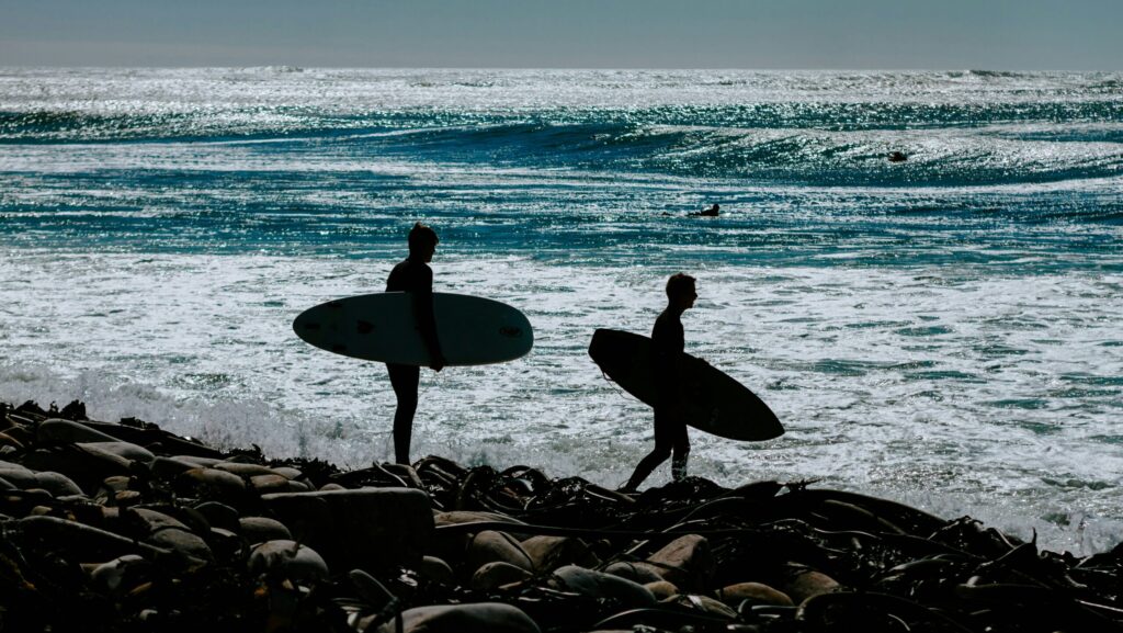 Two surfers holding their boards, standing on rocks, about to enter the ocean at Kommetjie surf, South Africa