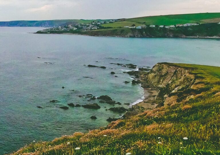 The ocean with cliffs on the left, grass on top, and cloudy skies at Bantham, South Devon, UK.