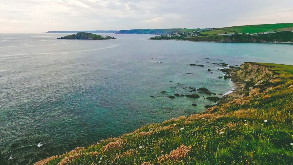 The ocean with cliffs on the left, grass on top, and cloudy skies at Bantham, South Devon, UK.