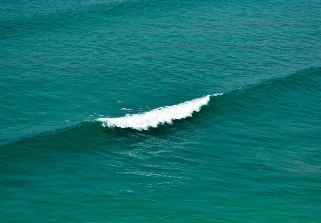 A gentle wave rolling in clear blue waters, with one wave recently broken and white water visible in Saunces surf, Spain