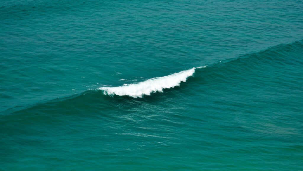 A gentle wave rolling in clear blue waters, with one wave recently broken and white water visible in Saunces surf, Spain