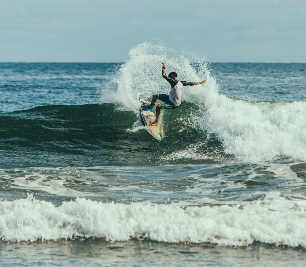 Surfer executes a powerful top turn with spray on a small wave under clear skies at Cimaja