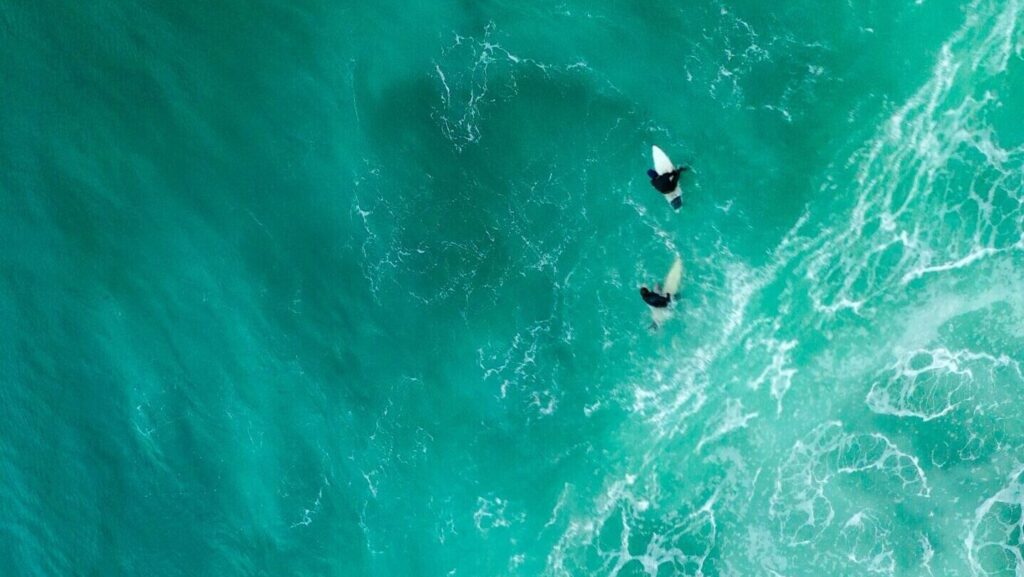 drone, bird's-eye view of three surfers in deep blue water at Zarautz Surf Beach, Spain