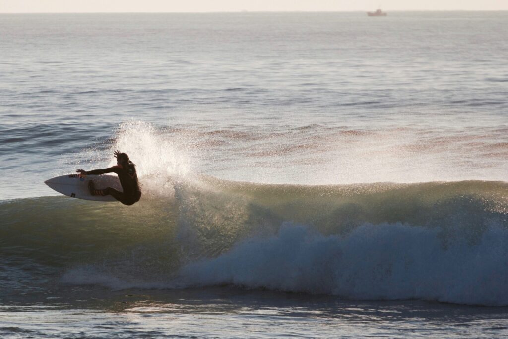 A surfer performing a powerful top turn on a right-hand wave, with sunlight reflecting on the water in Bantham Surf, United Kingdom