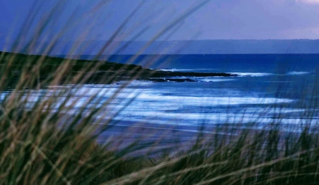 Croyde Bay Surf Beach, North Devon, at dusk with low light, grass in the foreground, and the beach and sea in the background