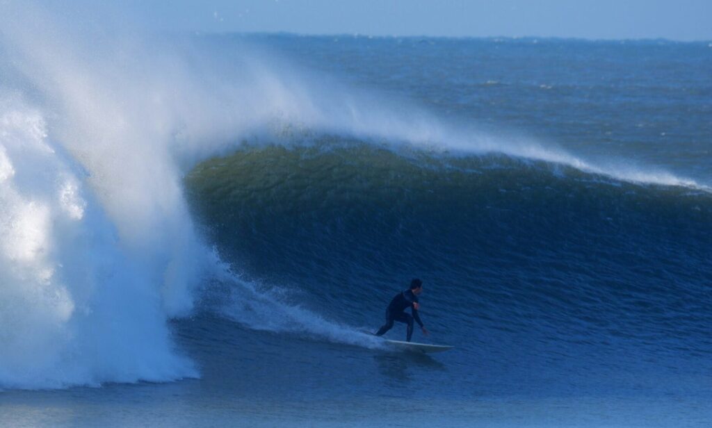 A surfer in a wetsuit doing a bottom turn on a big, perfect left-hand wave with offshore winds at Croyde Bay Surf, North Devon