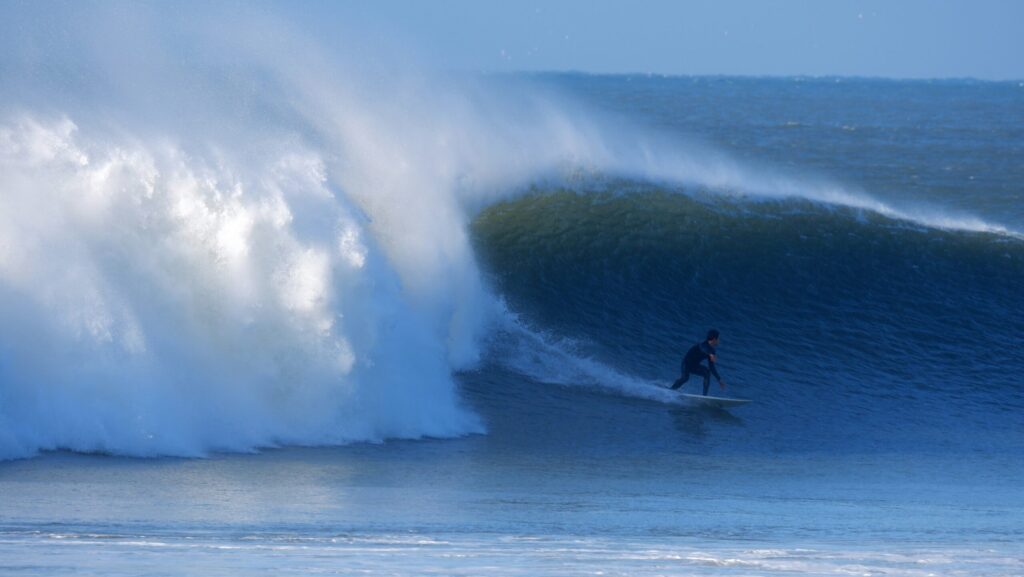 A surfer in a wetsuit doing a bottom turn on a big, perfect left-hand wave with offshore winds at Croyde Bay Surf, North Devon