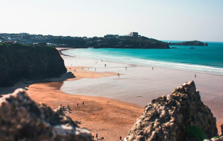 Newquay, England, with golden sandy beach, town in the background, and clear blue skies.