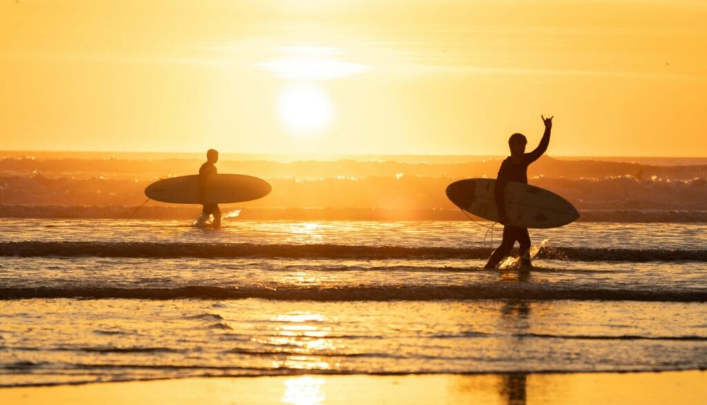 Two surfers exiting the water with the sun in the background, casting a yellow tint over the photo Barra de la Cruz surf, mexico