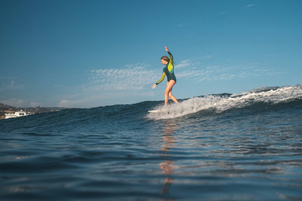 Water-level shot of a female surfer riding a mellow right-hand wave in Malibu, CA, dancing on her board under blue skies