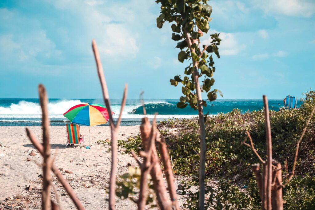 Perfect left-hand wave with a surfer in the barrel in the distance, colorful umbrella, and sand in the foreground at Lombok Surf, Indonesia