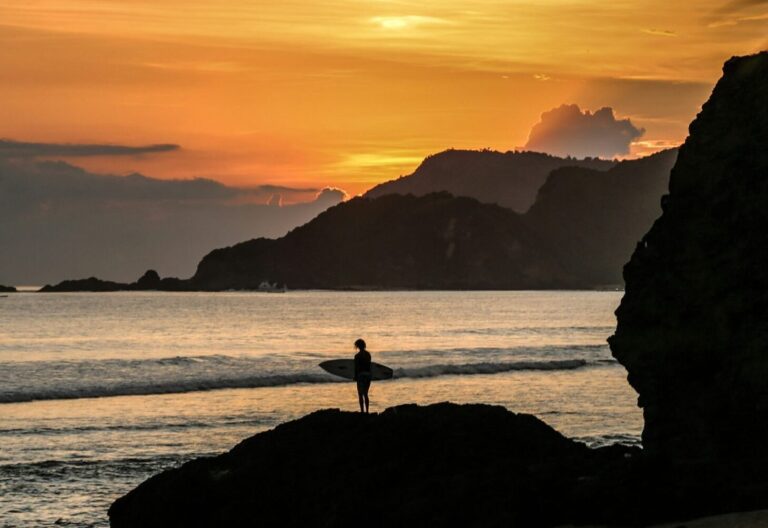 Man stands on the shore at Kuta Lombok, Indonesia, with a yellow sunset glow.