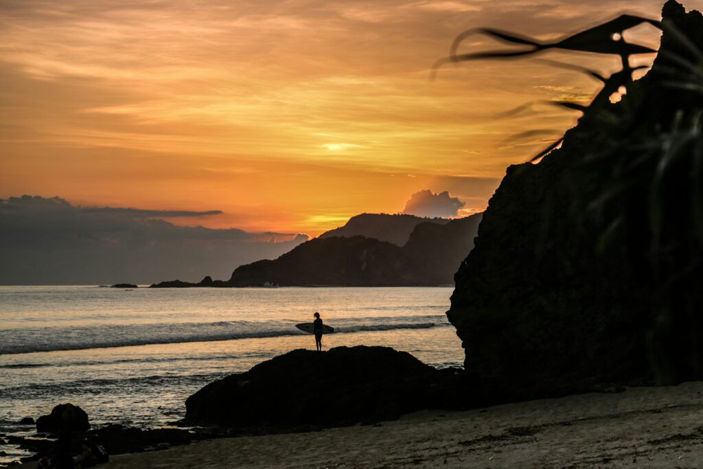 Man stands on the shore at Kuta Lombok, Indonesia, with a yellow sunset glow.