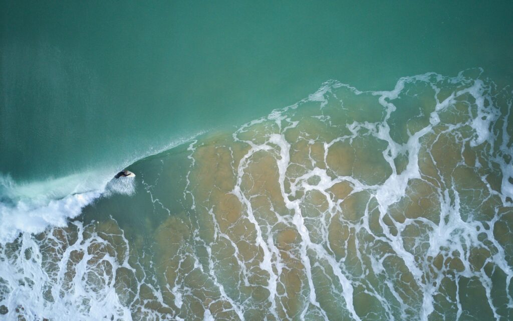 A drone view of a surfer in a barrel on a left-hand wave, with blue-grey water and sand visible in Suances surf, Spain