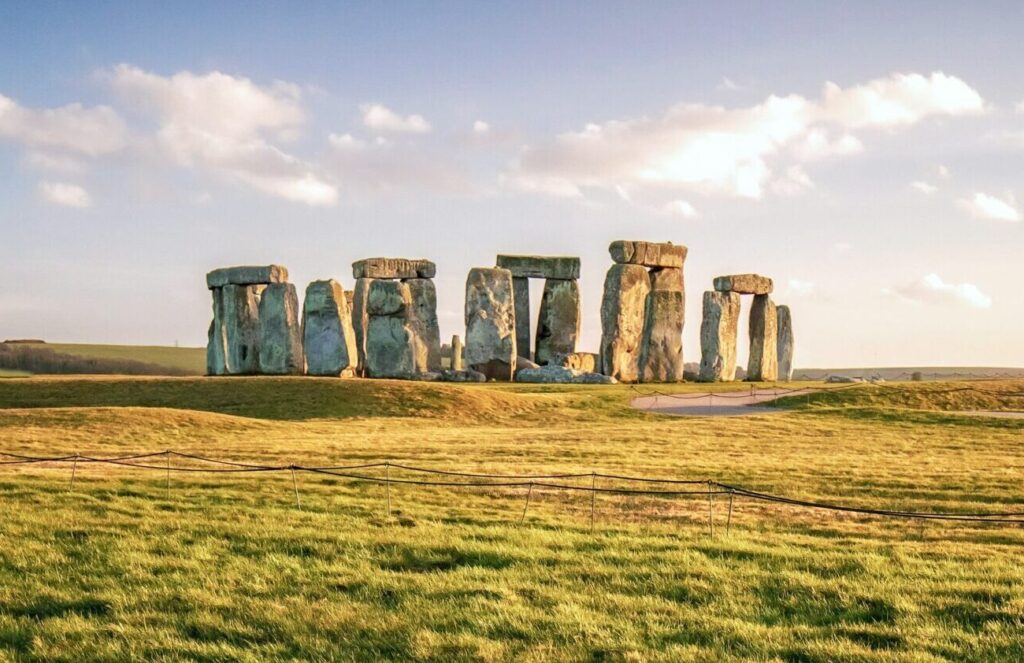 Stonehenge in Wiltshire, with bright green grass in the foreground, illuminated by sunlight and clear skies