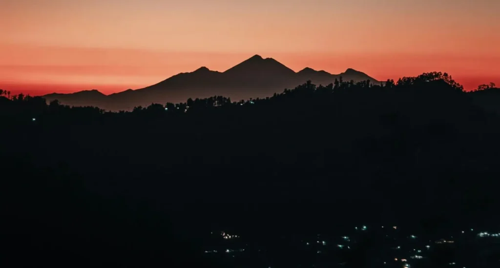 Denpasar at night with a mountain in the distance, red skies, and city lights.