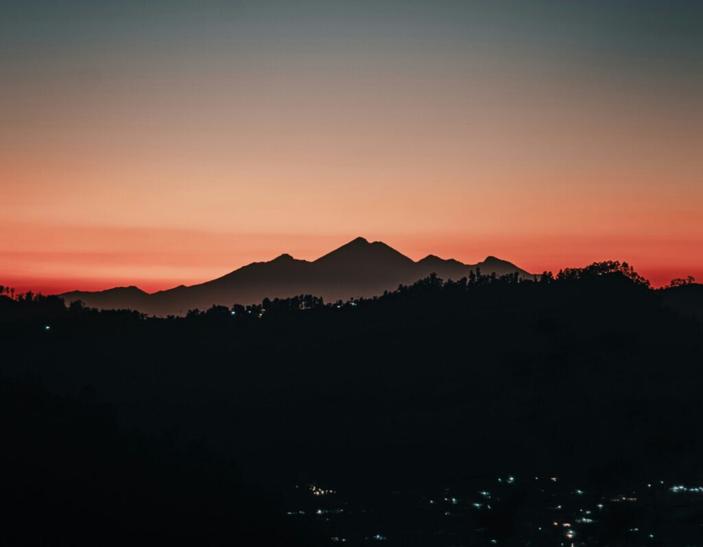 Denpasar at night with a mountain in the distance, red skies, and city lights.