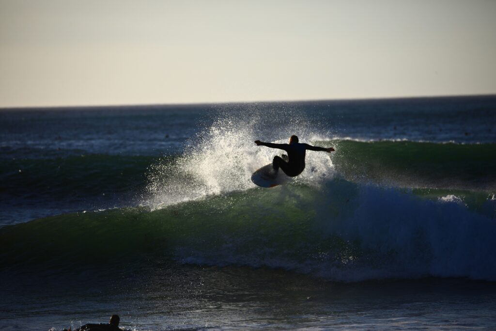 A surfer executing a huge turn in Kommetjie Surf with lots of spray and sunlight reflecting off the water