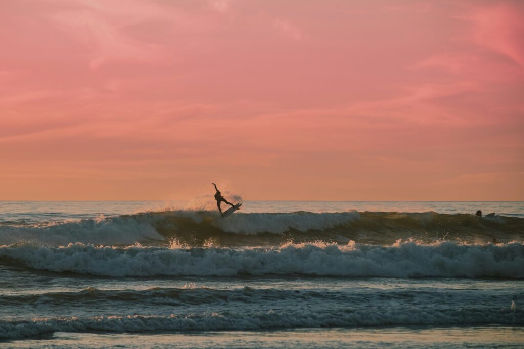 A surfer doing an air in Sennen Cove surf, UK, with a red orange sky