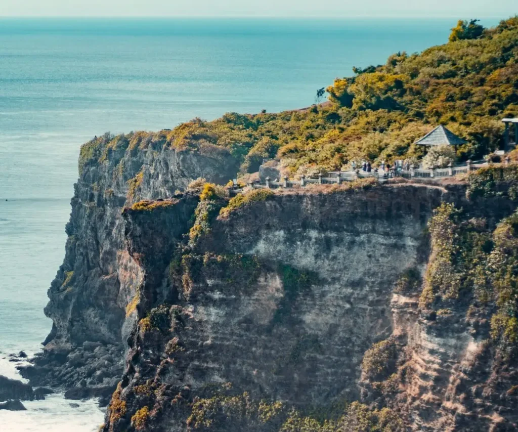 Uluwatu Temple on the cliff edge, with clear blue skies, long cliffs along the ocean, and blue water in the distance