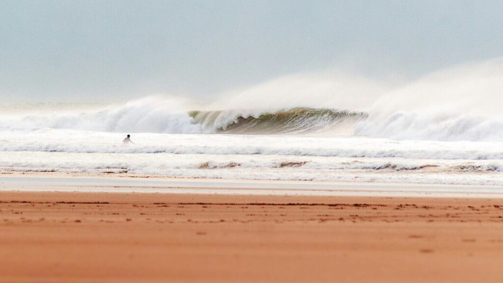 A big left-hand wave in the distance with sandy foreground and lots of white water at Croyde Bay Surf, North Devon.