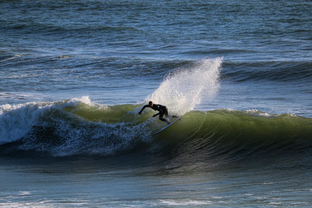 A surfer pulling off a backside turn with lots of spray and the sun reflecting off the water at Croyde Bay, North Devon