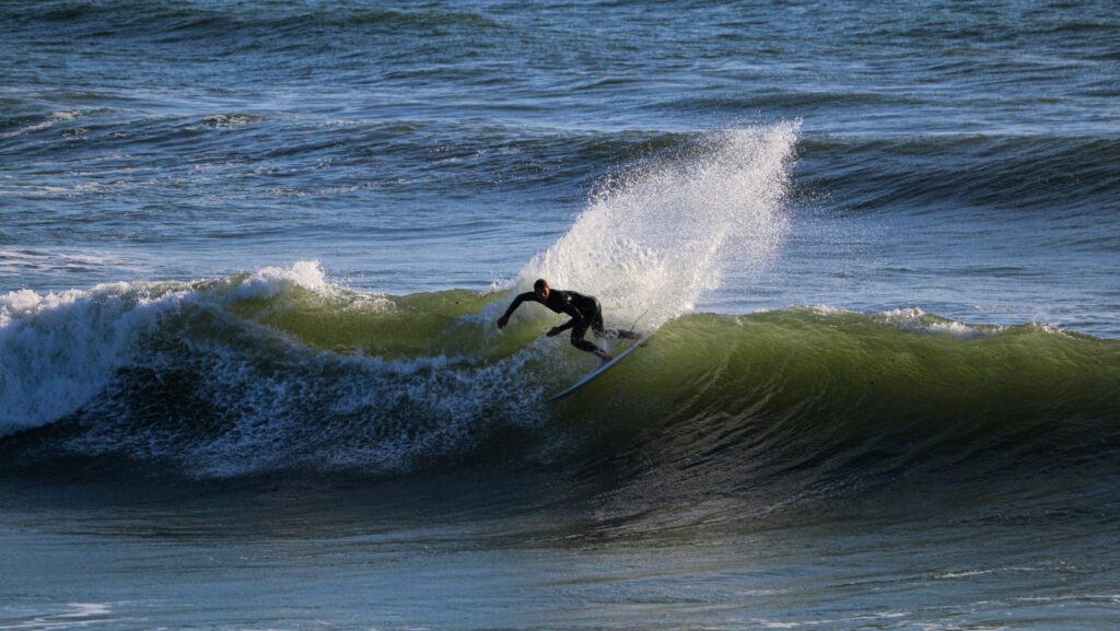 A surfer pulling off a backside turn with lots of spray and the sun reflecting off the water at Croyde Bay surf, North Devon