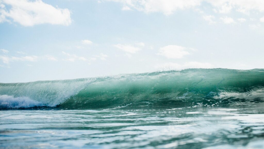 A blue left-hand wave breaking with a barrel, set against a clear blue sky, photographed from the water in Saunces surf, Spain