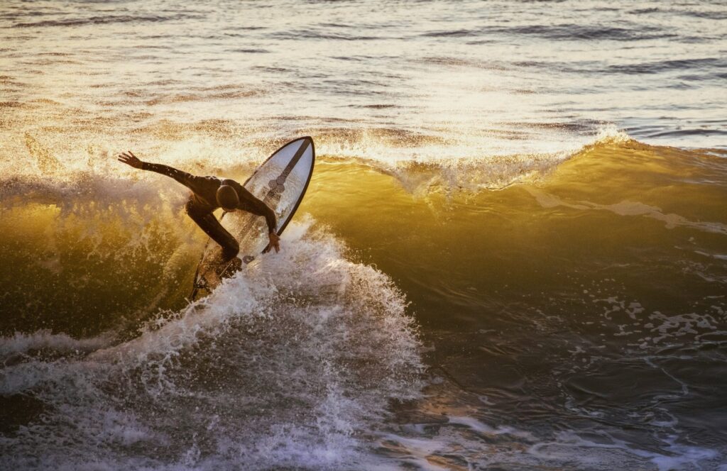 A surfer performing a top turn on a left-hand wave with sunlight reflecting on the water in Mundaka Surf, Spain