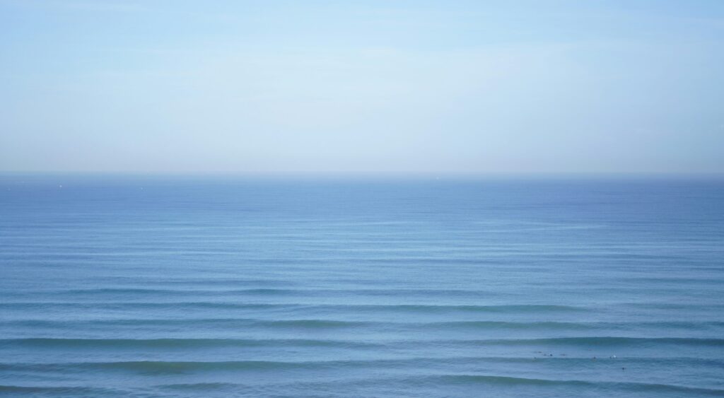 A view looking out into the ocean at Gijon Surf, Asturias, featuring endless waves on the horizon under clear blue skies