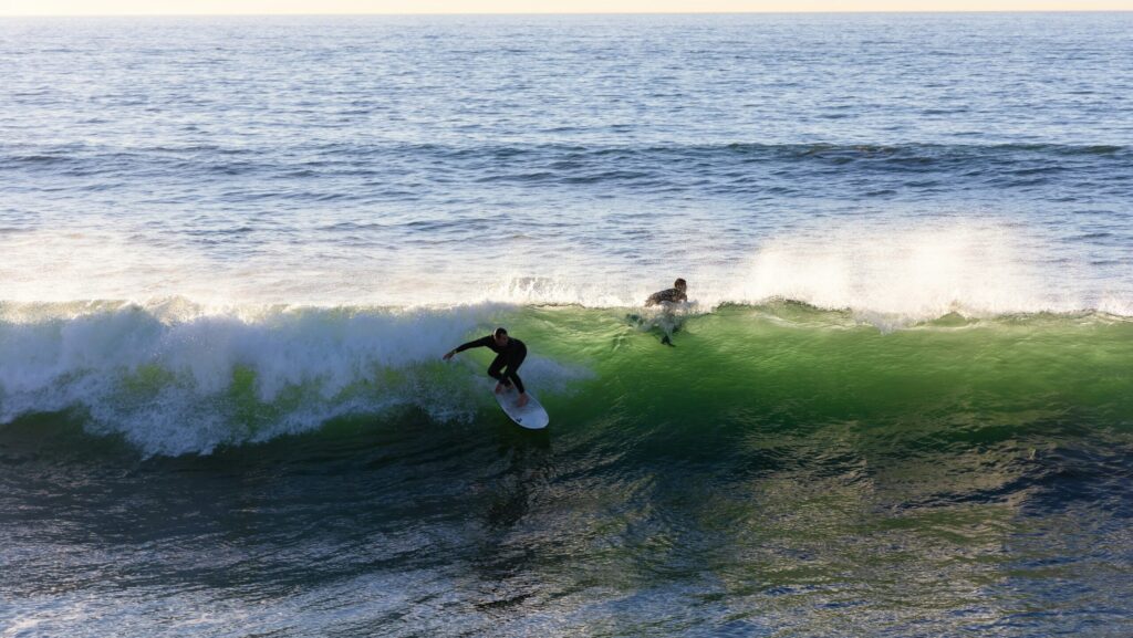 A surfer taking off on a left-hand wave with the surf in Perranporth surf, UK