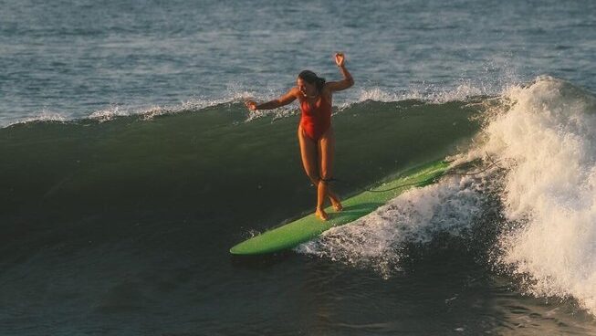 A girl surfing on a Malibu in Playa Las Flores surf in El Salvador with SurfXplore