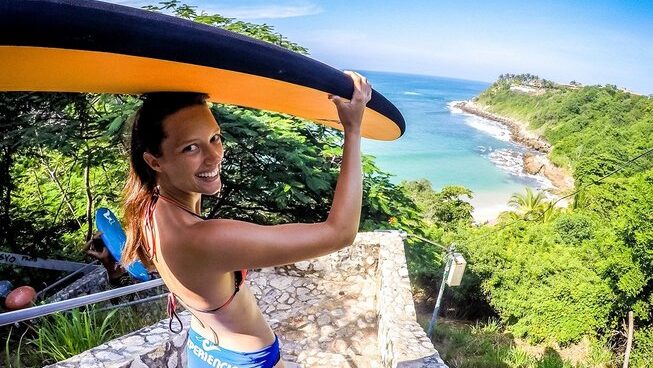 A girl walking to the surf with a surfboard on her head at Puerto Escondido with Image Credit: Experiencia Puerto Escondido