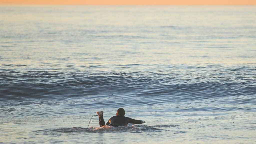 Victoria Bay surf at sunset with a surfer paddling