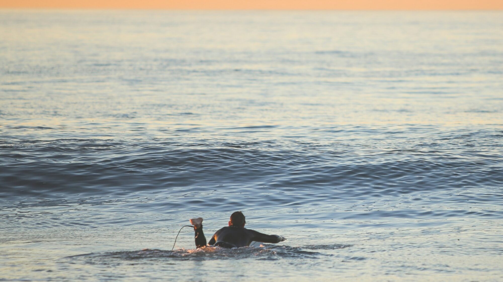 Victoria Bay surf at sunset with a surfer paddling