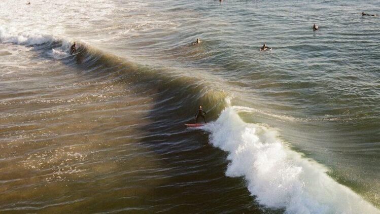 Two surfers surfing one wave at Huntington Beach surf Pier in California