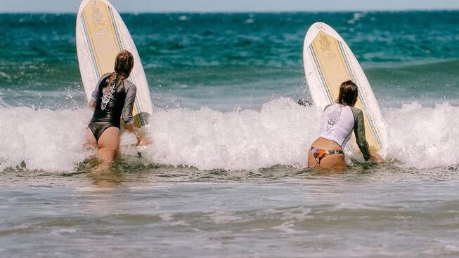 Two girls going out into the ocean with Iguana Surf Camp in Tamarindo surf camp