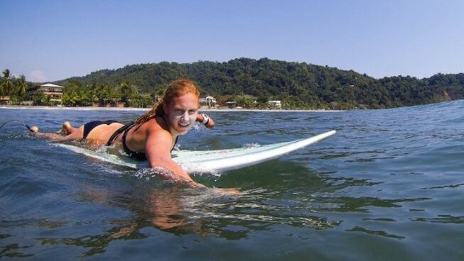 A girl paddling on a surfboard with clear blue skies at Photographers all taking a photo at accommodation at Jaco surf camp with school of the world