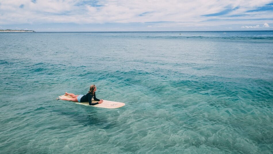 A girl laying on a surfboard in blue water with Yoga Surf Retreat Portugal Algarve