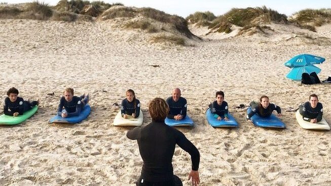 People laying on a surfboard on the sand at Peniche Portugal with Ahoy Surf House surf camp