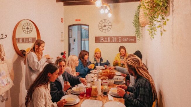 people sitting around a table and eating dinner at Balili Beach House surf camp in Peniche Porutgal