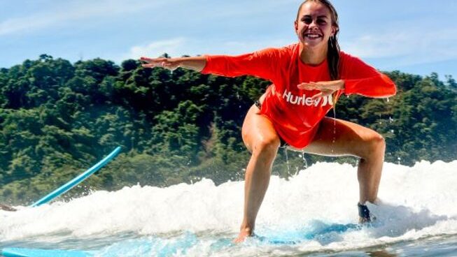 A learner surfer standing up on a wave at Damo Surf Camp in Jaco