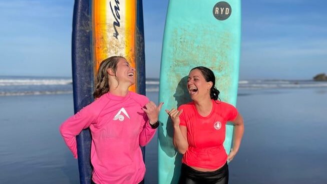 Two people laughing and holding surfboards behind them at Del Alma Retreat Costa Rica surf camp