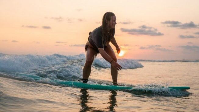 A learner surfer at sunset standing on a wave at Global Surf Lodge Kabalana Surf Camp
