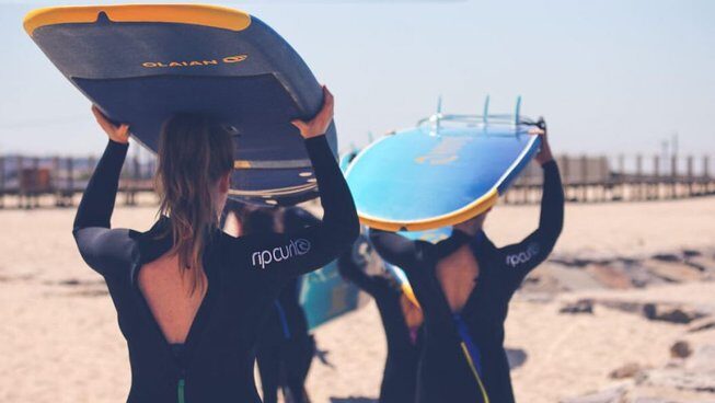 people carrying surfboards on their head at Golden Waves Surf and Yoga Lodge surf camp Portugal