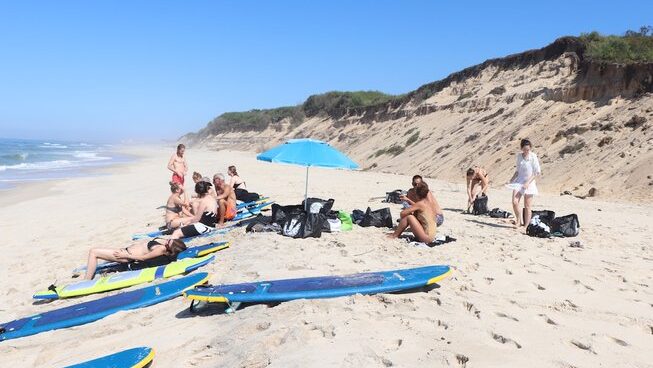 People sitting by the beach with umbrella and surfboard at Golden Waves Surf and Yoga Lodge camp in Portugal