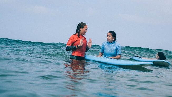 A surf instructor talking to a learner surf in the water at Good People Surf surf camp in Zarautz